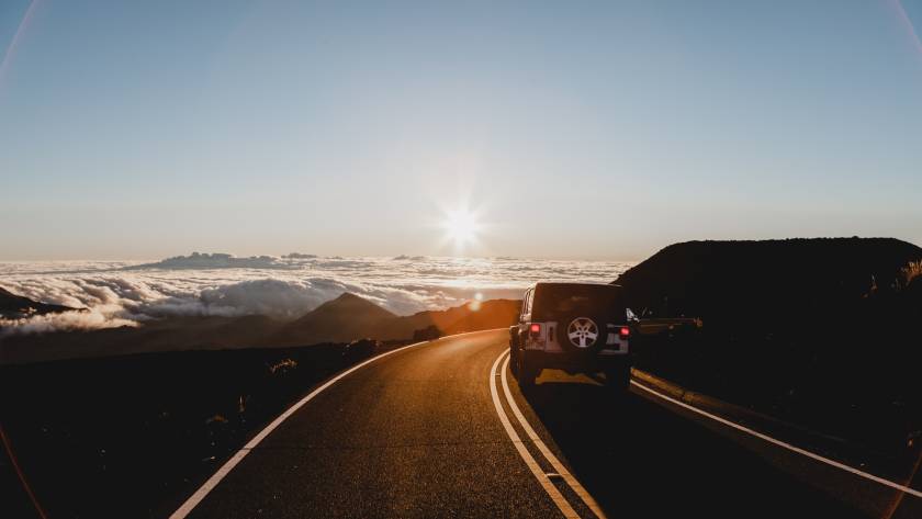 Car driving on a scenic mountain road during sunrise above the clouds in a tranquil landscape setting