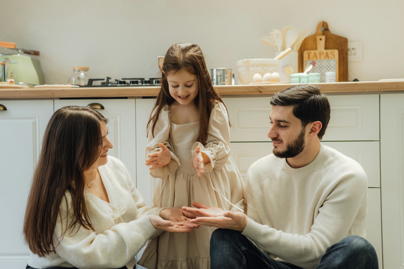 Family playing together in a cosy kitchen, wearing matching cream-coloured outfits and enjoying a joyful moment