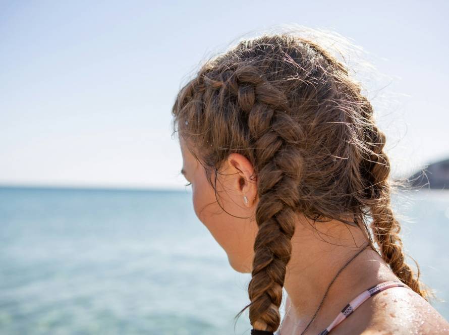 Young woman with braided hair enjoying a sunny beach view near the ocean
