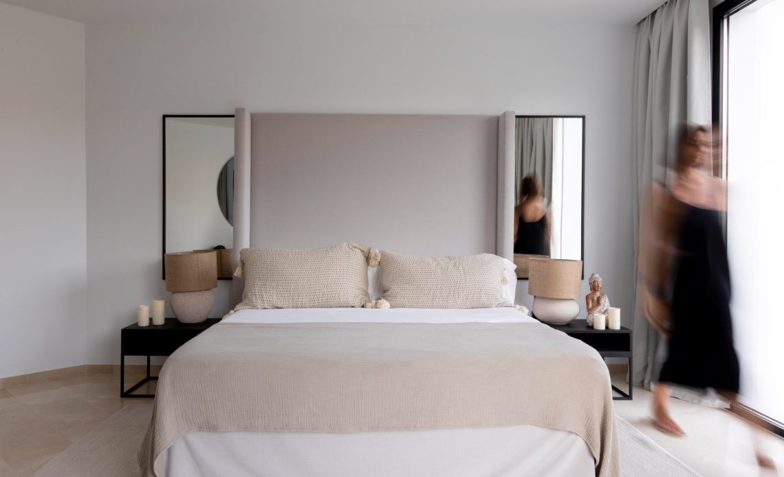 A woman strolls through a bedroom with a bed and mirror, highlighting the room's elegant decor and personal touch