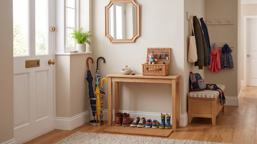Bright hallway with wooden table, wicker basket, shoes, umbrellas, coats, and a plant near the window for home decor